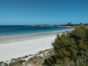 A beach with clear blue water, white sand, and sparse vegetation. - Maison Près de la Mer/plage (Plougoulm)