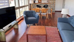 Una sala de estar moderna con televisor, sillones azules, una mesa de centro de madera y un comedor con salpicadero de piedra.