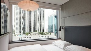 Habitación de hotel con un ventanal grande, una cama y vistas de edificios altos.