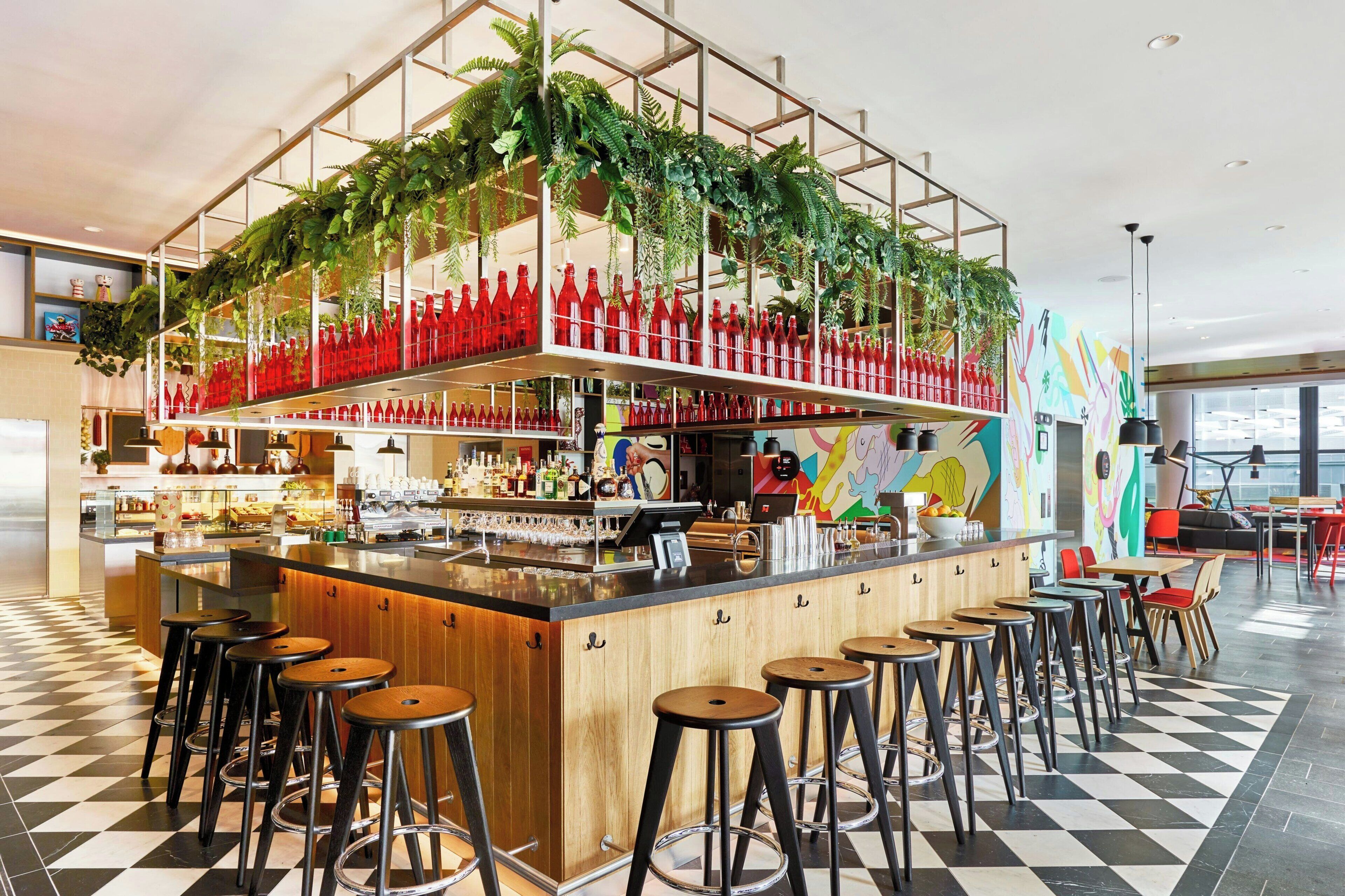 A bar area with a checkered floor, wooden stools, and a bar counter with a variety of bottles and glasses.