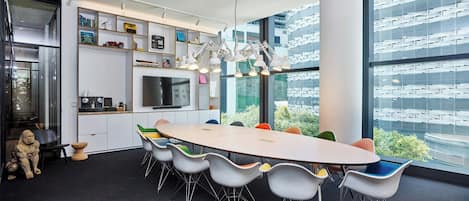 A modern conference room with a large oval table, colorful chairs, a whiteboard, and a large window offering a view of a building.