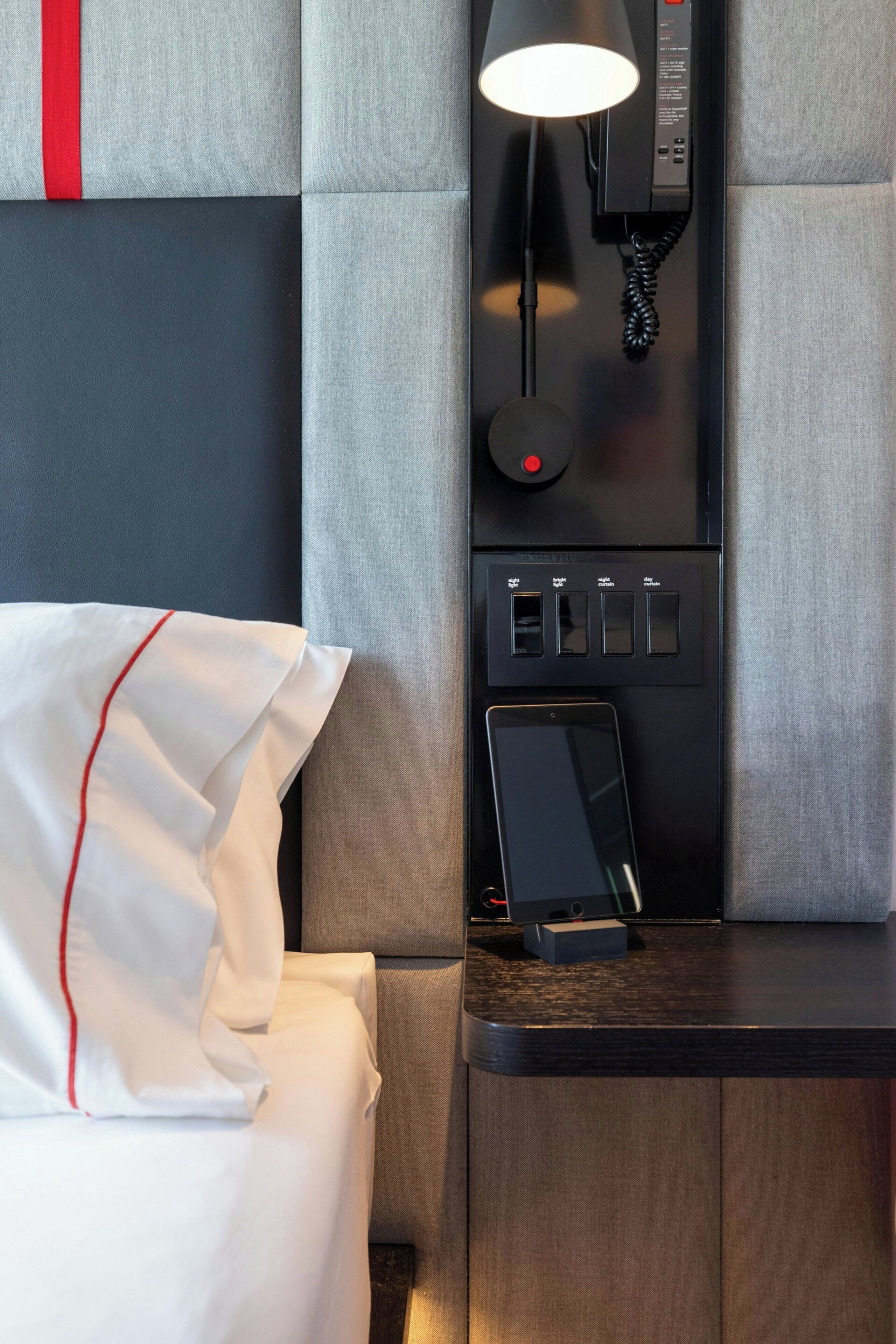 Una habitación de hotel con una cama, una mesita de noche con un teléfono y un teléfono en la pared.
