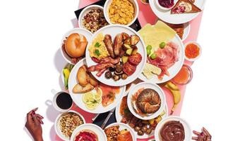 A variety of breakfast foods arranged on a table, including toast, eggs, sausages, and fruits.