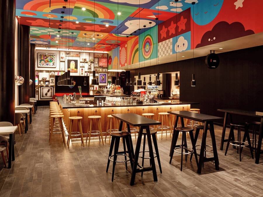 Zona de bar moderna con techo colorido, taburetes de madera y barra.