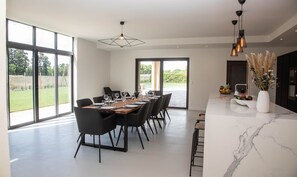 A modern dining area with a large table set for six, black chairs, and a view of the outdoors through large windows.