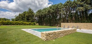 A rectangular swimming pool with stone walls, surrounded by a well-maintained lawn and a stone wall with lounge chairs. - Mas des Lilens (L'Isle-sur-la-Sorgue)
