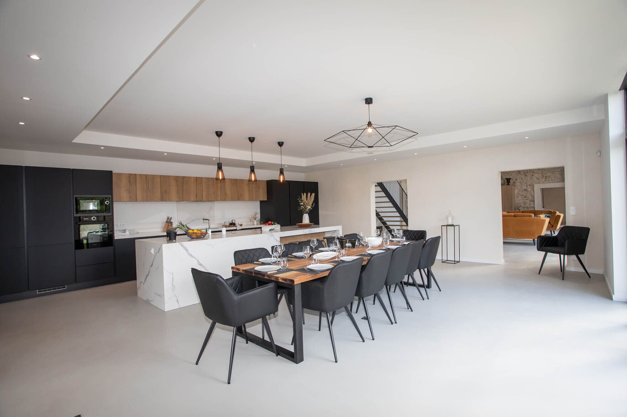 A modern kitchen with a central island, black chairs, and a dining table set for six.