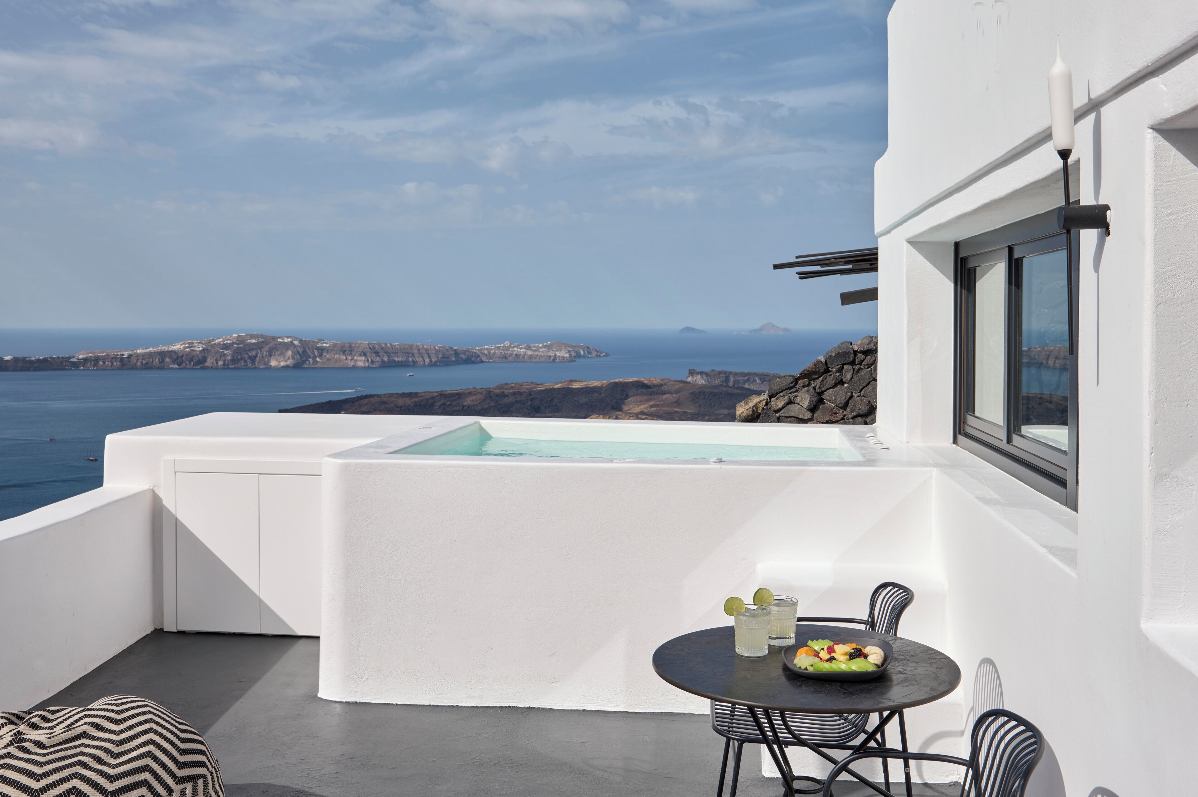 A balcony with a table, chairs, and a view of the sea and cliffs.