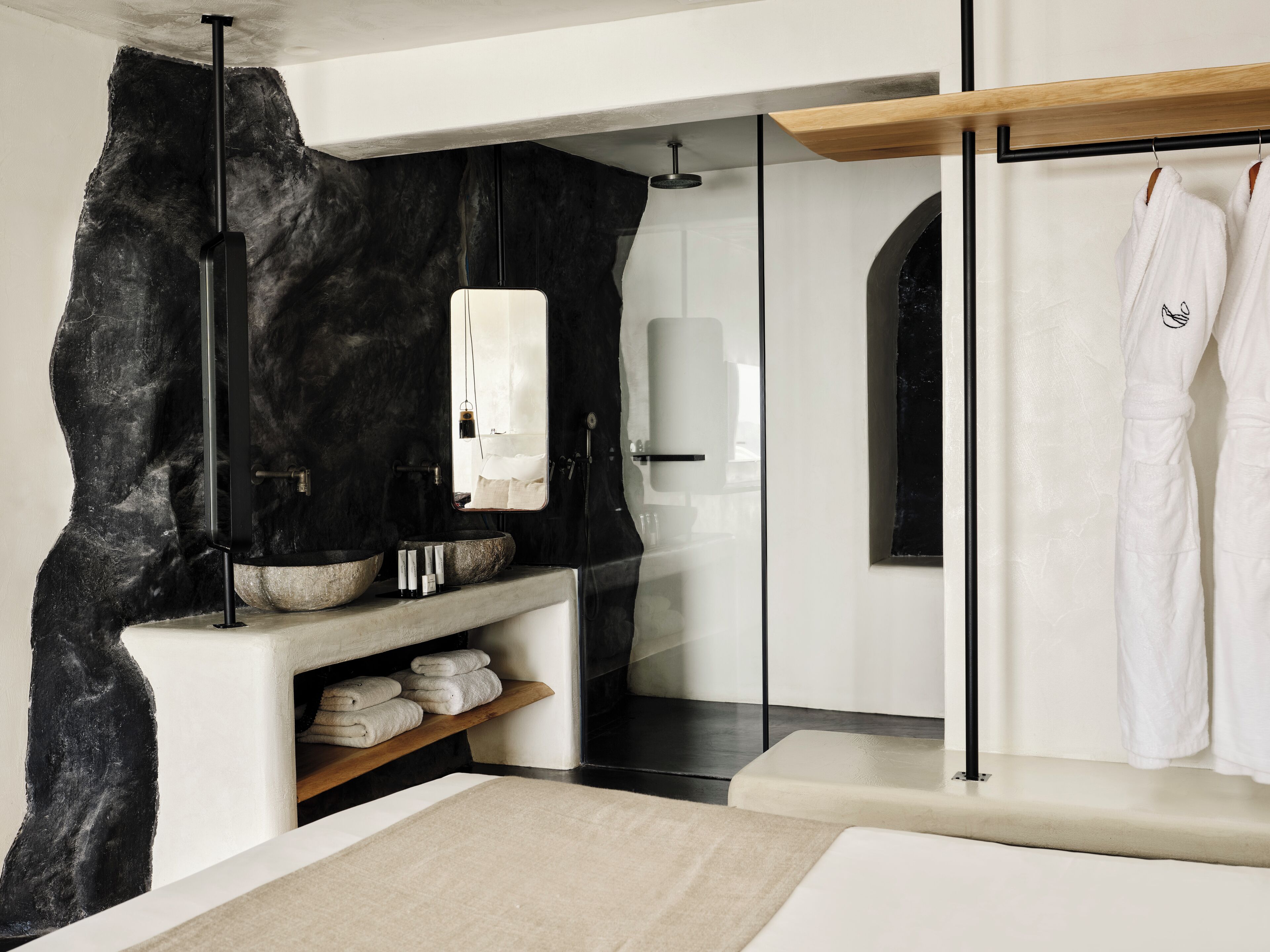 A modern bathroom with a stone accent wall, a glass shower enclosure, and a wooden shelf with towels.