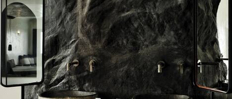 A bathroom with a large mirror, two stone sinks, and a stone basin.