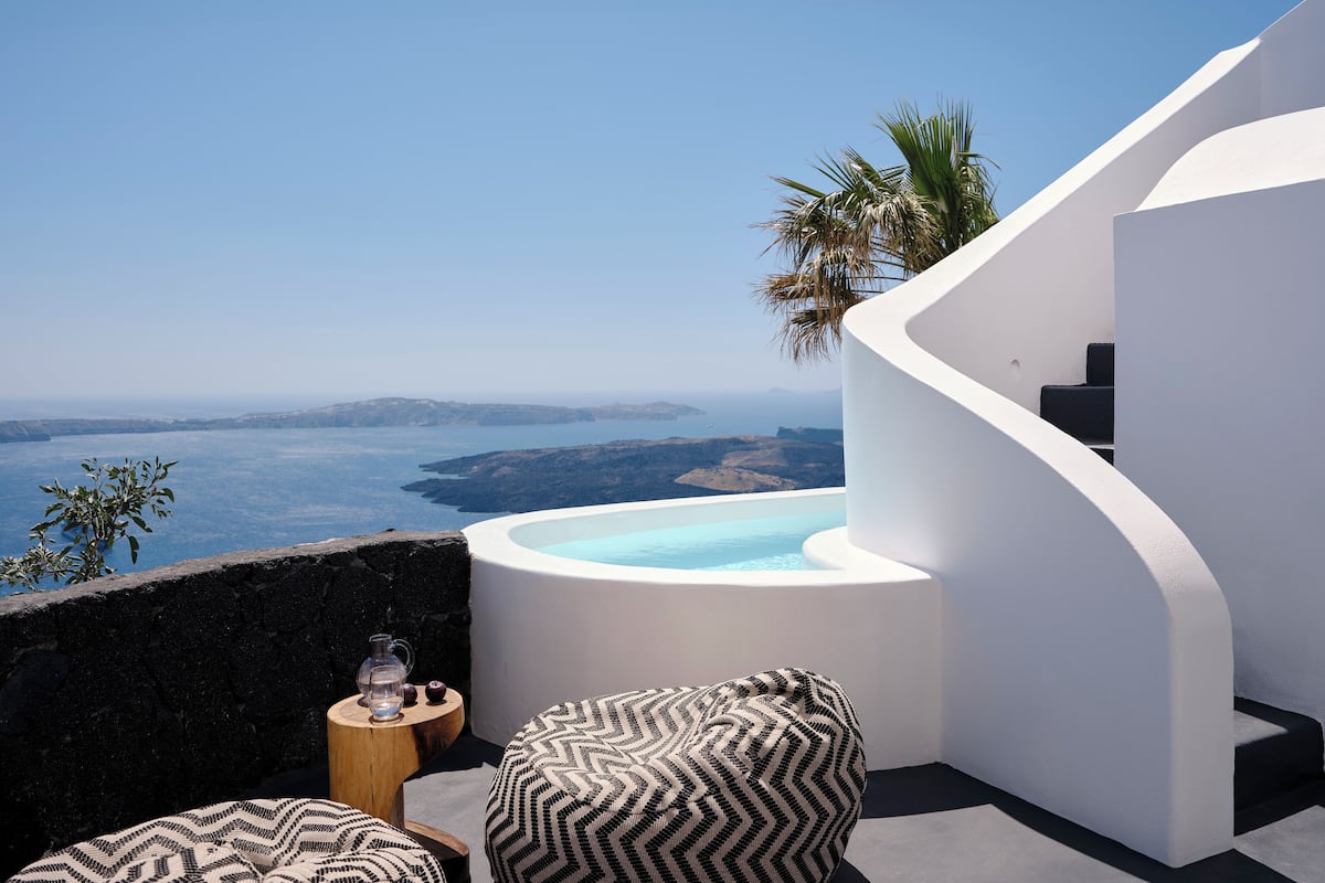 A modern outdoor seating area with a pool, overlooking a scenic view of the sea and hills.