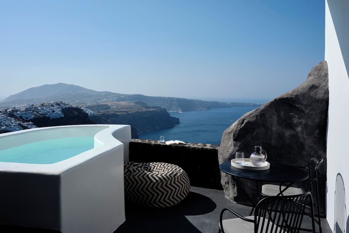 A balcony with a view of the sea, a hot tub, and a table with a glass and book.