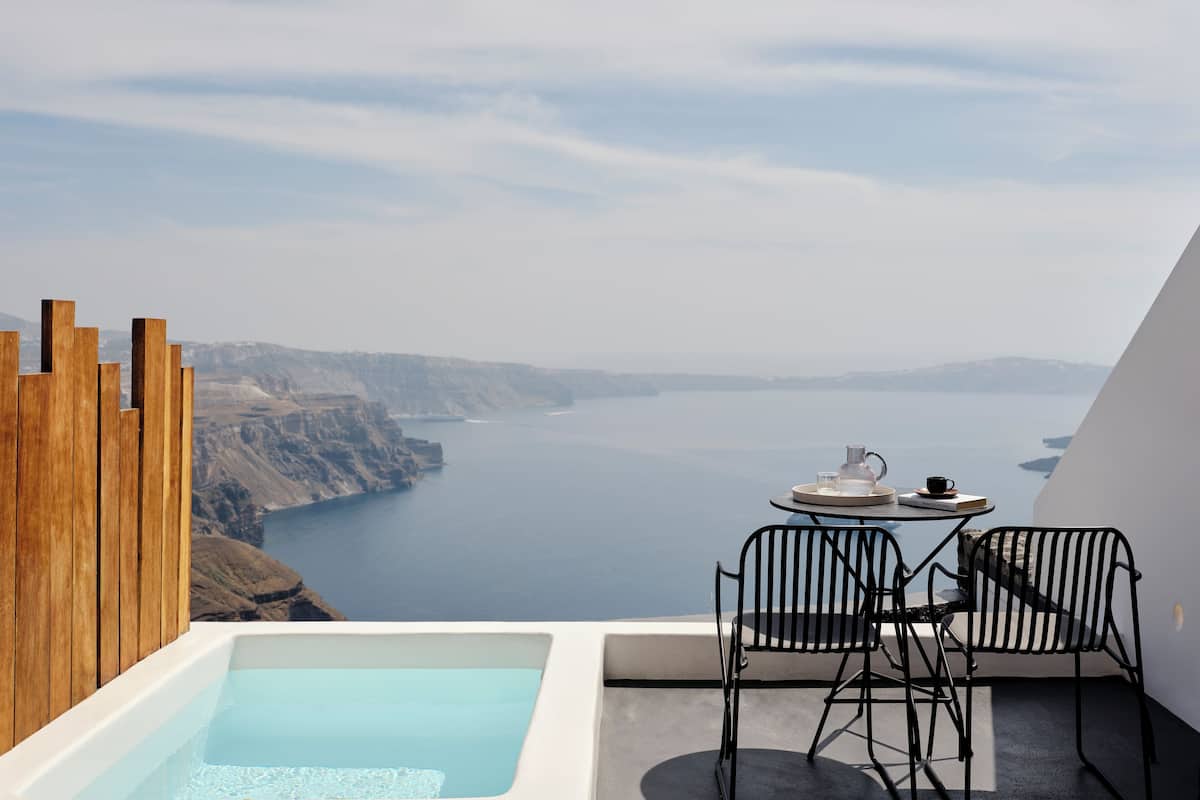 A balcony with a view of a large body of water, wooden slats, a small table with chairs, and a hot tub.