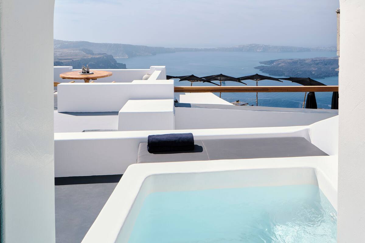 A rooftop terrace with a view of the sea and mountains, featuring a pool and outdoor seating.