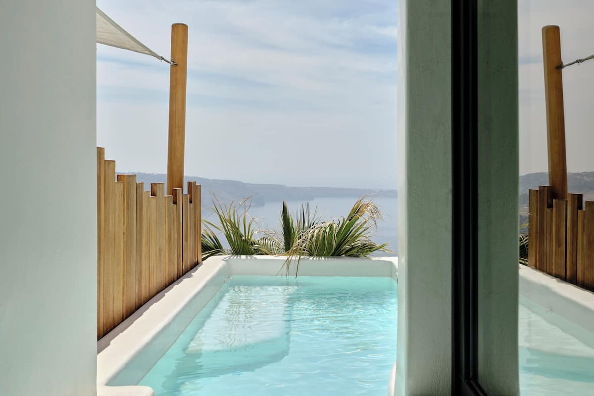 A pool with a view of the sea and mountains, surrounded by wooden fences and plants.