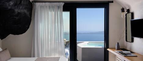 Habitación de hotel moderna con una cama grande, un escritorio con computadora, vista al mar y un jacuzzi.
