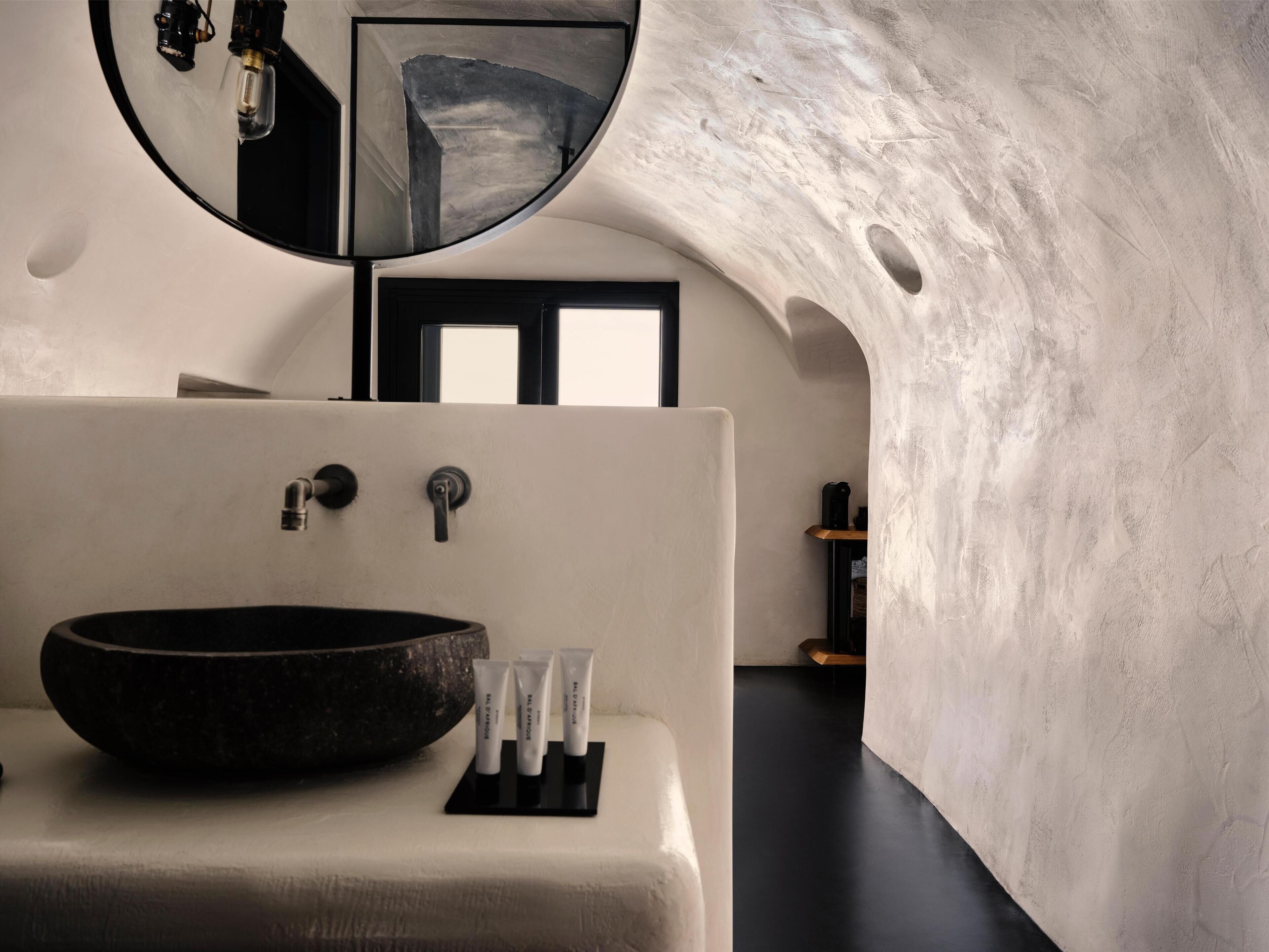 A modern bathroom with a large round sink, a mirror, and a door leading to another room.