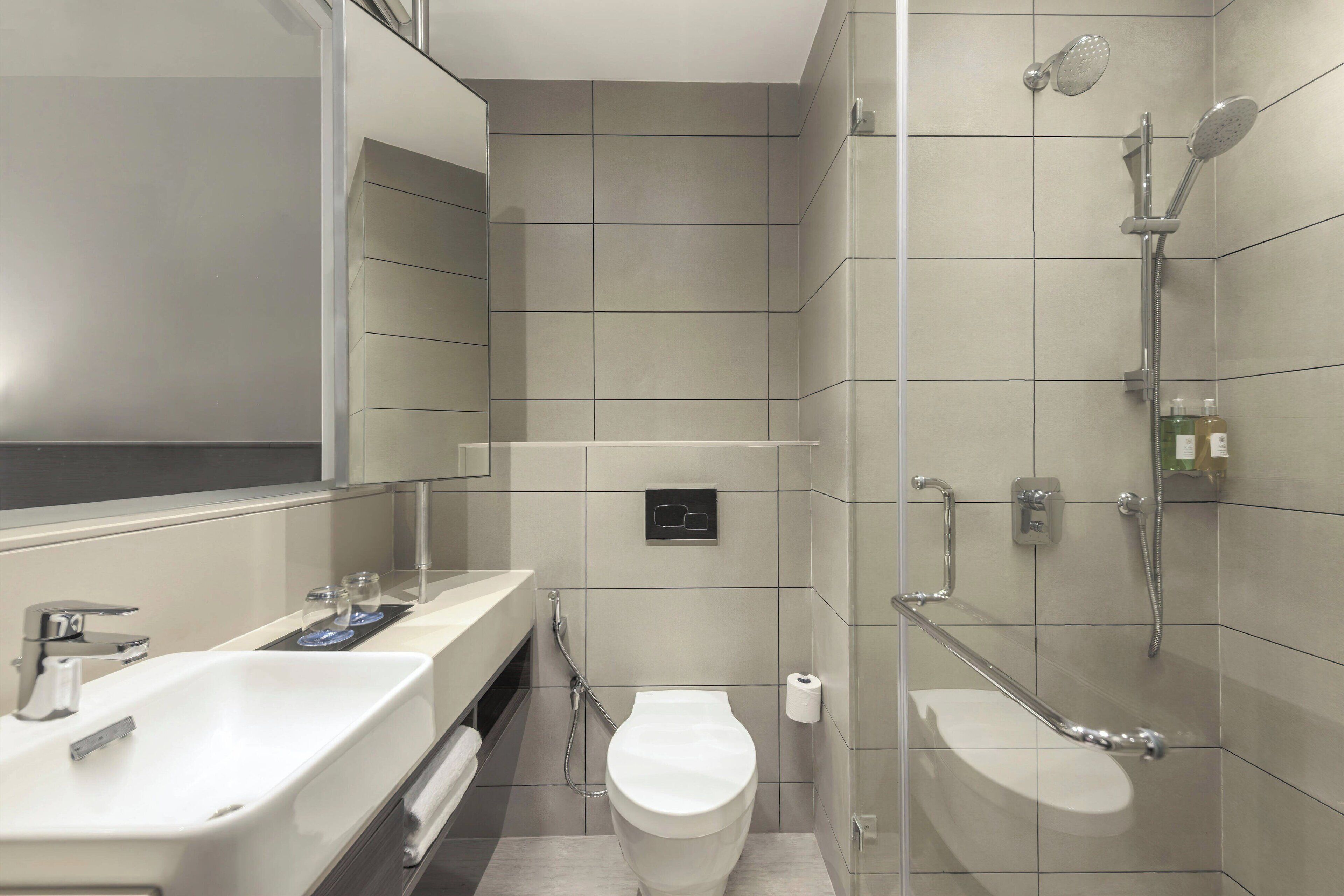 A modern bathroom with a large mirror, a sink, a toilet, and a shower area.