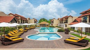 A swimming pool surrounded by lounge chairs and umbrellas, with a clear sky and buildings in the background. - Fairfield by Marriott Goa Benaulim (Benaulim)