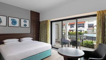 Habitación de hotel con cama, una mesita y balcón con sillas y vista a la piscina.