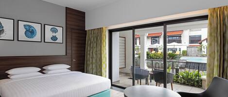 A hotel room with a bed, a small table, and a balcony with chairs and a pool view.