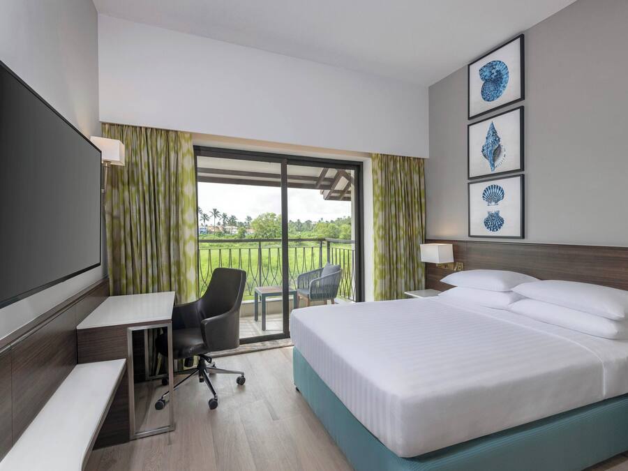 Habitación de hotel con cama, escritorio, silla y un ventanal con cortinas.