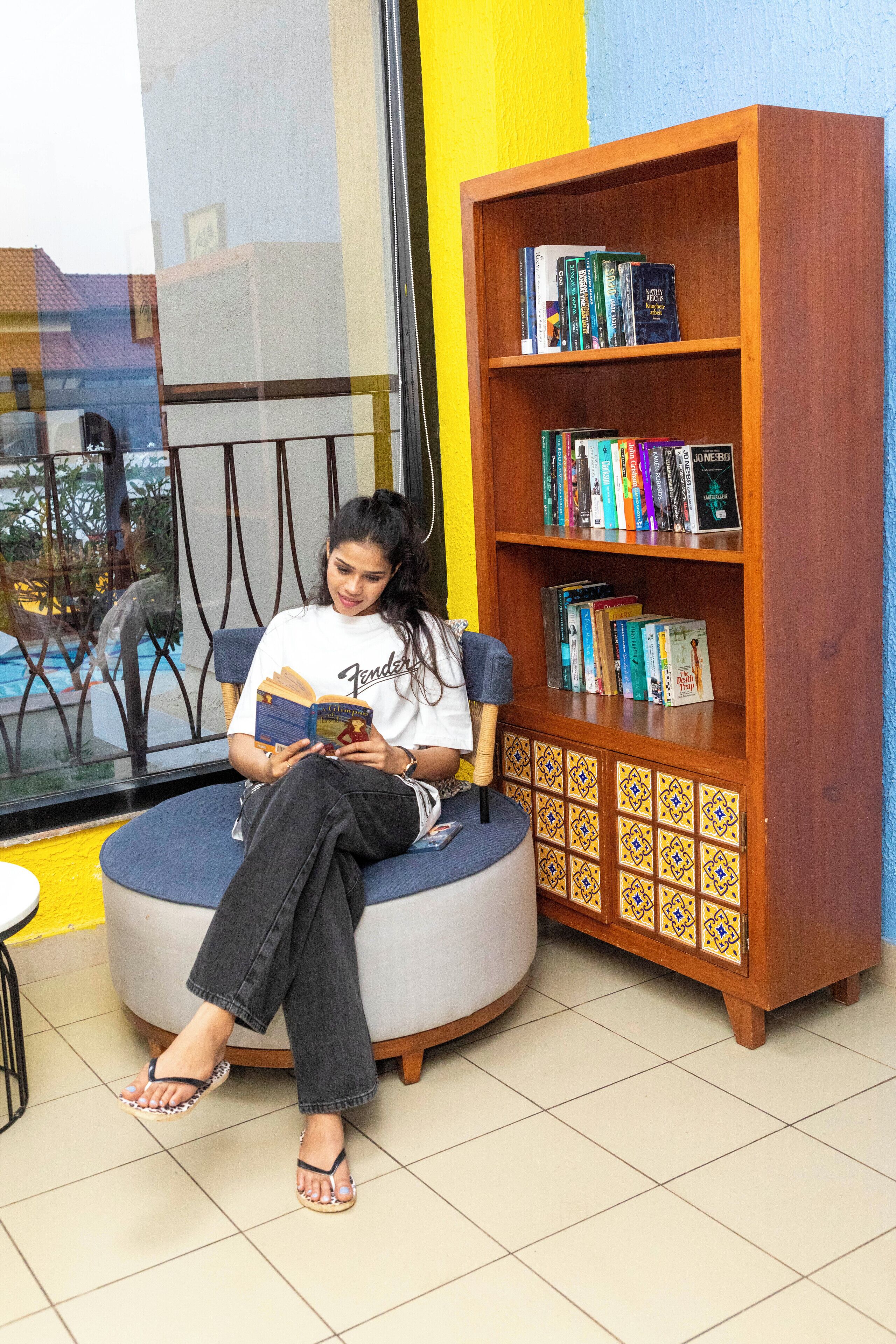 A person sitting on a round chair reading a book, with a bookshelf nearby.