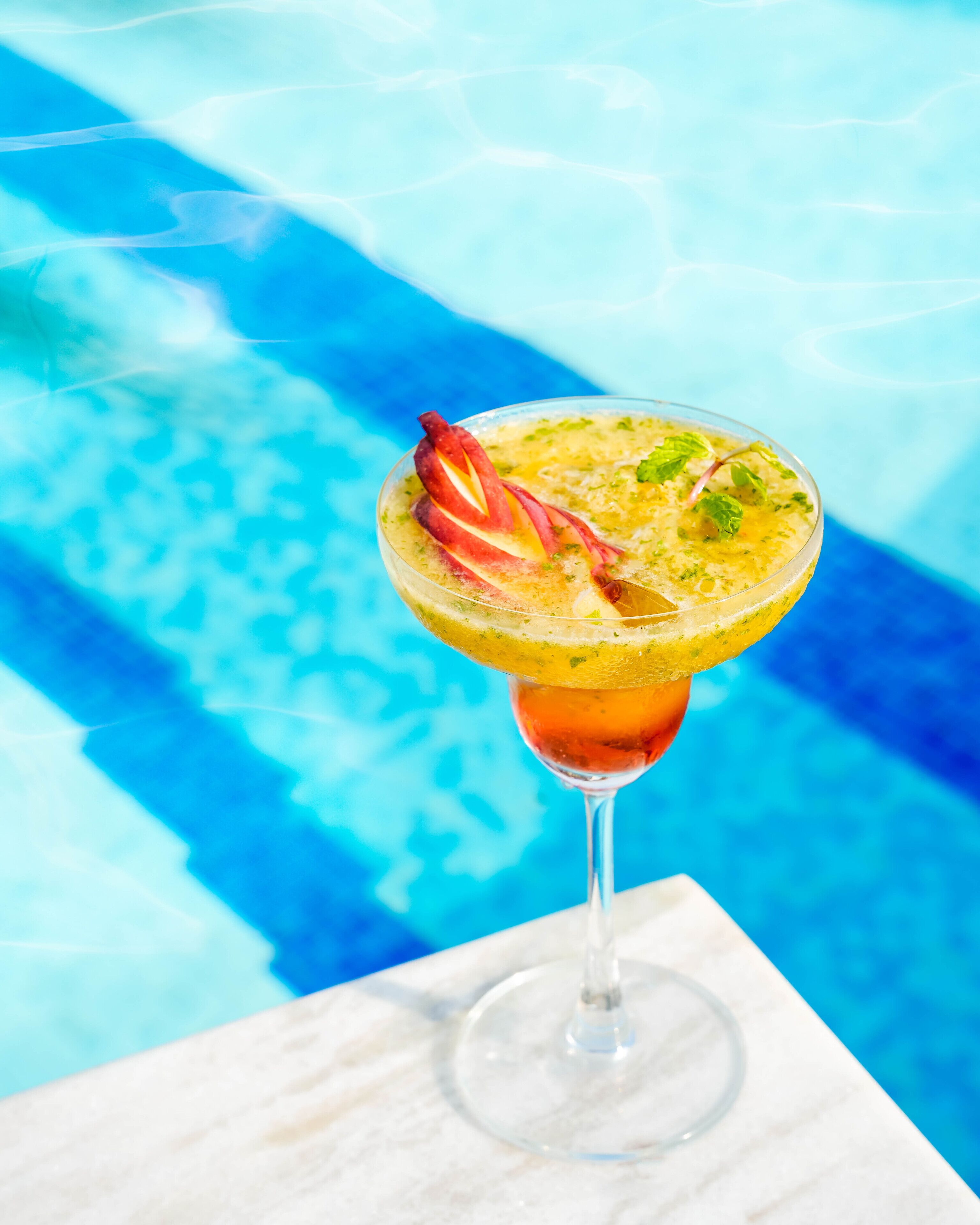 Un cóctel en una copa de martini con un adorno decorativo, frente a una piscina.