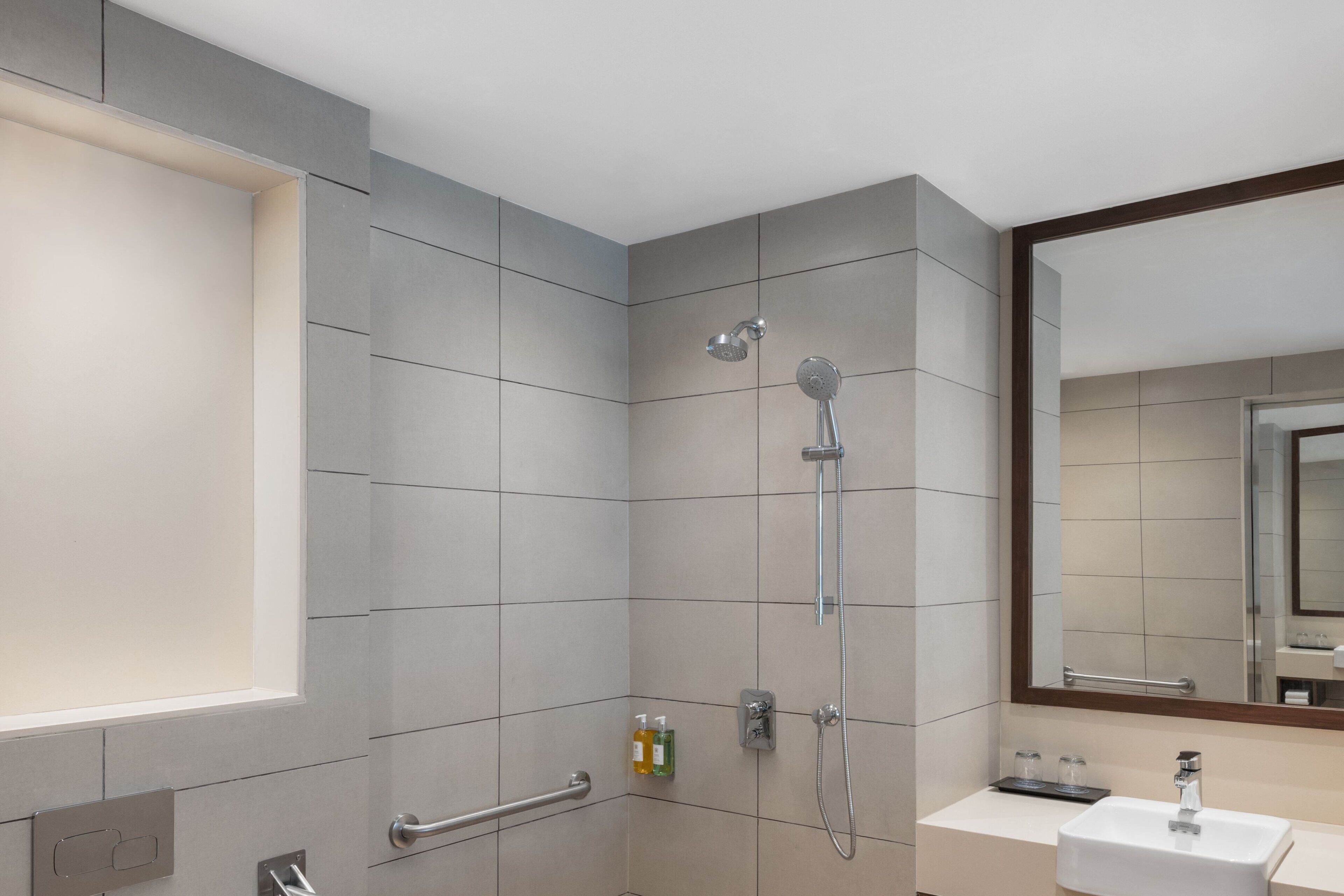 Un baño moderno con azulejos grises, ducha, lavamanos y espejo.