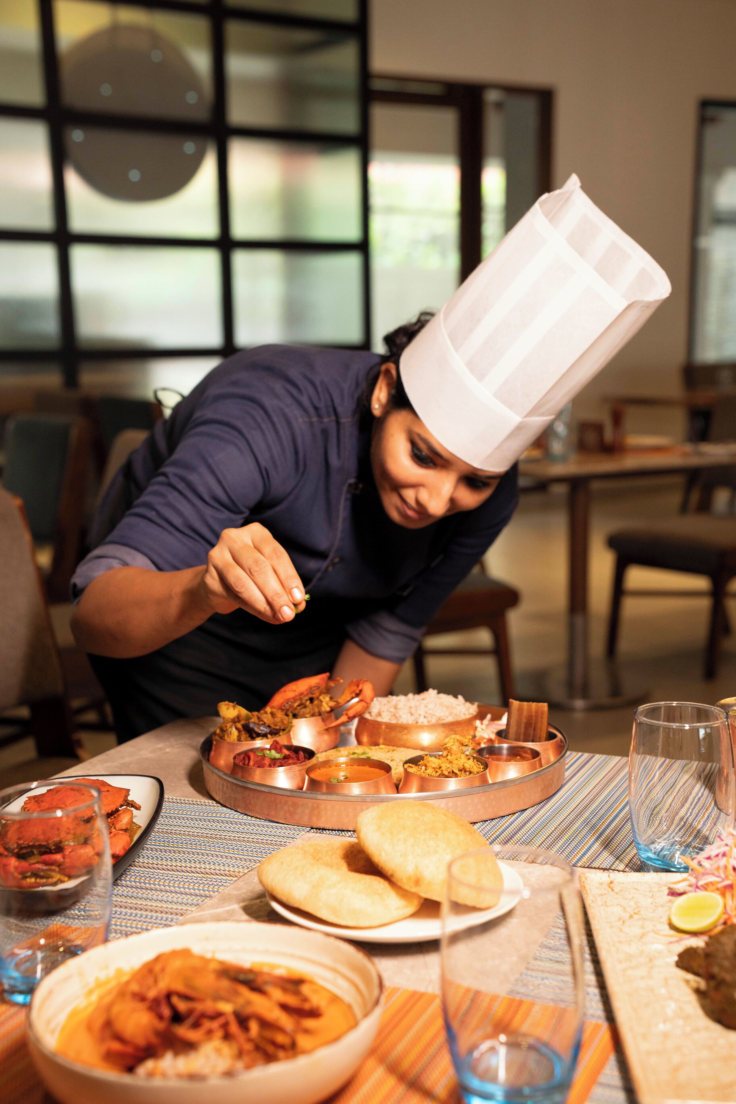 A chef serving food at a table with various dishes and a glass of blue liquid.