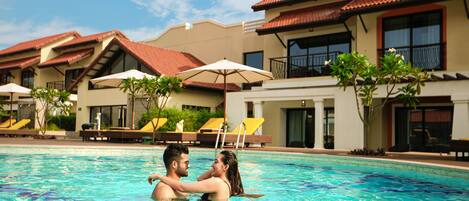 A couple in a swimming pool with a resort building in the background.