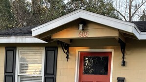A house with a red door, number 608, a small porch with steps, and a white birdcage on the wall.