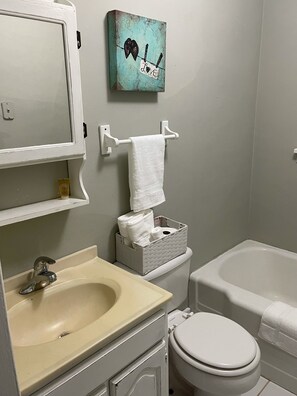 Une salle de bain équipée d’un lavabo, de toilettes et d’une baignoire. On y trouve un porte-serviettes sur lequel est accrochée une serviette blanche.