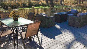 A deck with a glass-top table and chairs, surrounded by wicker seating and a wooden fence. - Sophisticated Lenox Retreat by Evergreen Home (Lenox)