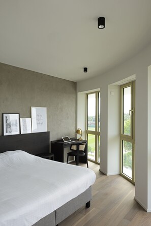 A modern bedroom with a large bed, a desk with a laptop, and a view of greenery through large windows. - Parkhotel Waregem (Waregem)