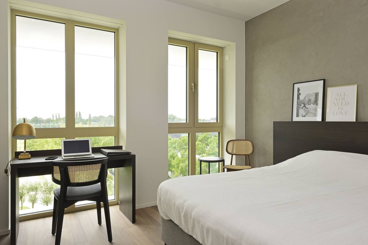 A bedroom with a bed, a desk with a laptop, and two chairs.