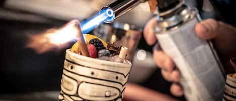 A person using a blowtorch to heat a beverage in a decorative cup.