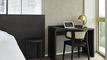 A modern bedroom with a bed, a desk with a laptop, a chair, and framed inspirational quotes on the wall.