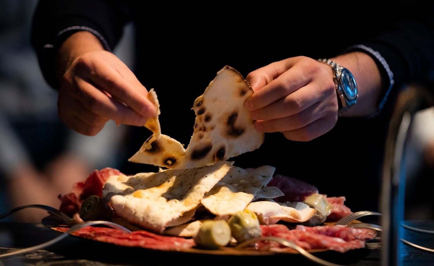 Una persona sosteniendo un pan plano, con un plato de comida al frente.