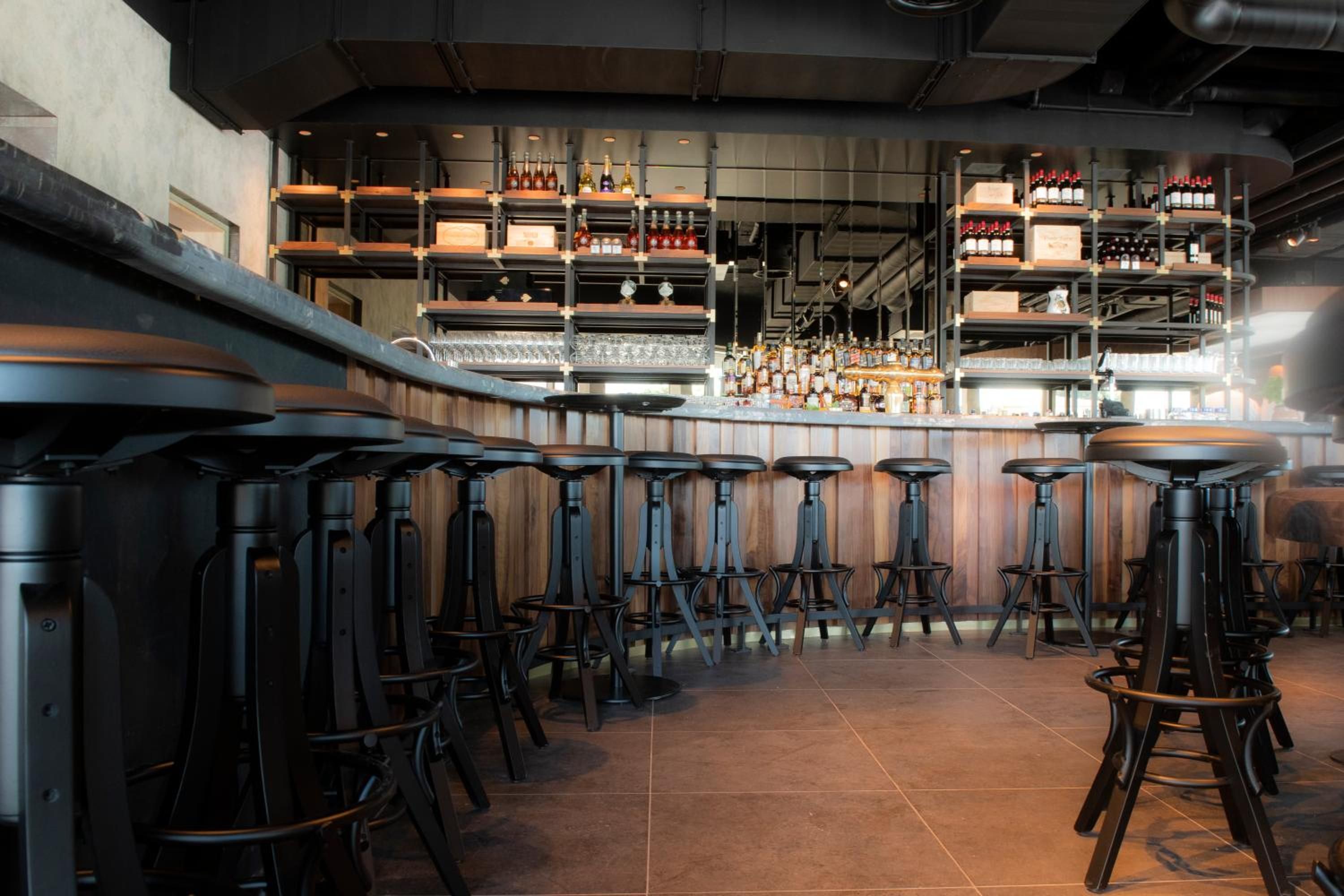 Zona de bar con varios taburetes y estanterías llenas de botellas.