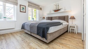 A bedroom with a large bed, two bedside tables, a window with curtains, and a shelf with decorative items. - fewo1846 - Hugo Eckener / centrally located maisonette apt. on the 1st floor (Flensburg)