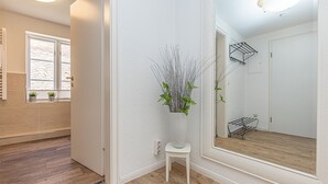 A clean, modern bathroom with a wooden floor, a white wall, a large mirror, and a small white stool. - fewo1846 - Hugo Eckener / centrally located maisonette apt. on the 1st floor (Flensburg)