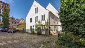 A white building with a cobblestone driveway, a parking sign, and a tree with green leaves.