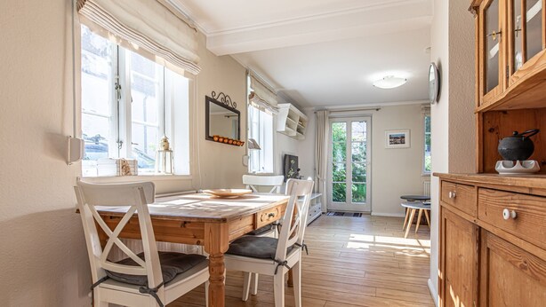 A dining area with a wooden table and chairs, a window with curtains, and a kitchen area with wooden cabinets.