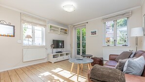 A living room with a brown leather sofa, a round coffee table, a flat-screen TV, and a bookshelf.