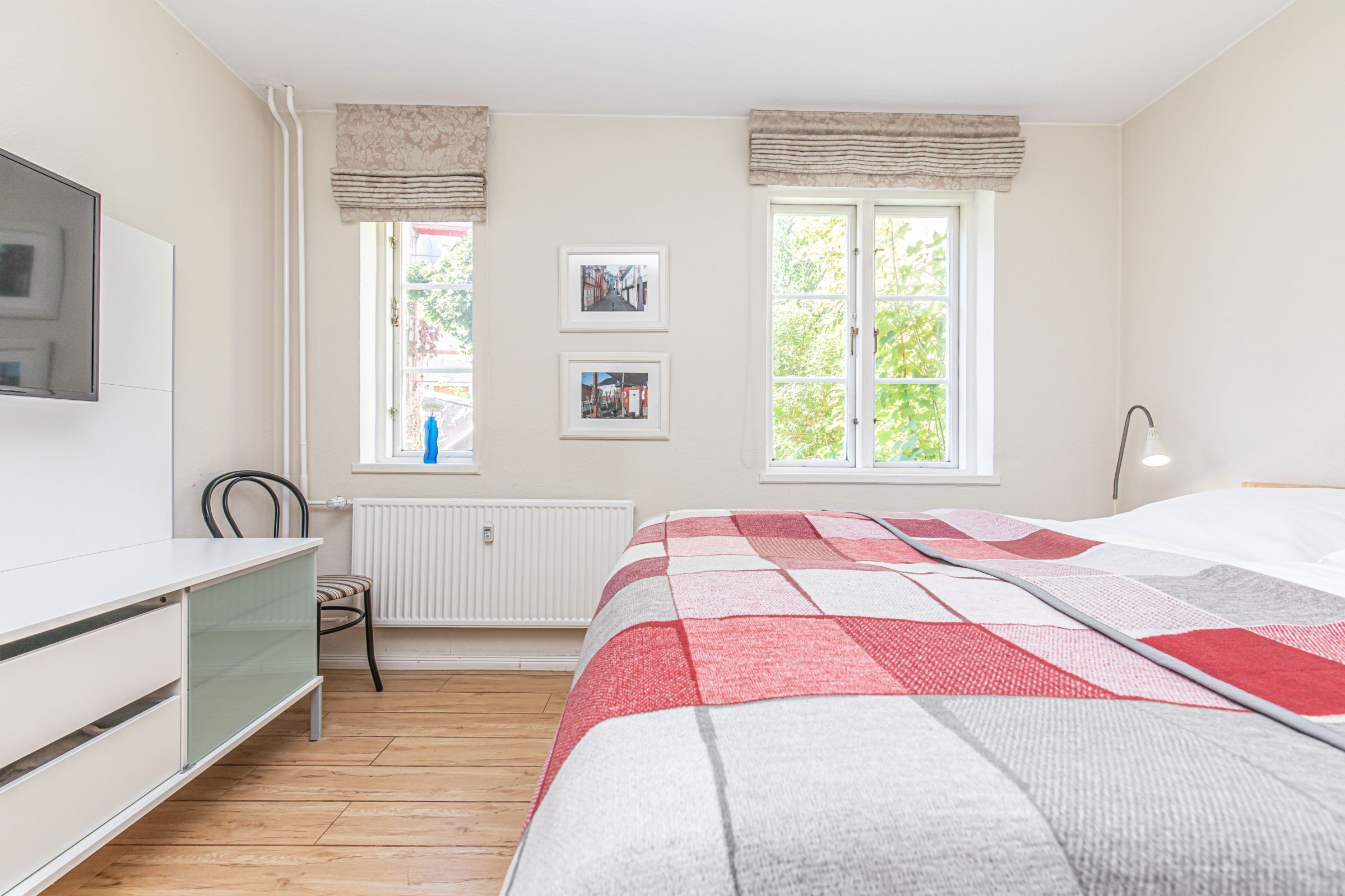 A bedroom with a bed, a desk, a chair, two windows, and a radiator.