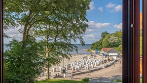 A beach with a row of beach huts, a pathway, and a building in the background. - fewo1846 - Marina del Rey (App. 146) / Studio App. with sea view and beach chair (Glücksburg)