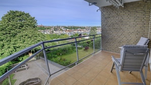 A balcony with a view of a town, a carport with two cars, and a grey chair.