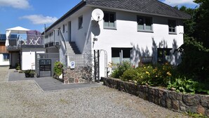 A white building with a satellite dish, a gated entrance, and a stone wall with plants.