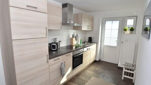 A modern kitchen with light wood cabinets, stainless steel appliances, and a window with potted plants.